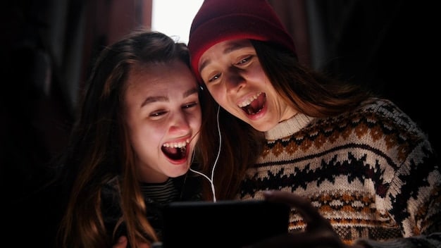 Two friends sitting on a couch, one holding a tablet and showing something funny to the other, who is laughing and pointing at the screen. The room is cozy and well-lit.