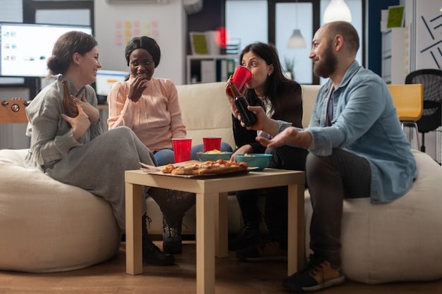 A group of friends laughing and clapping while playing a board game around a table in a brightly lit living room. Snacks and drinks are on the table.