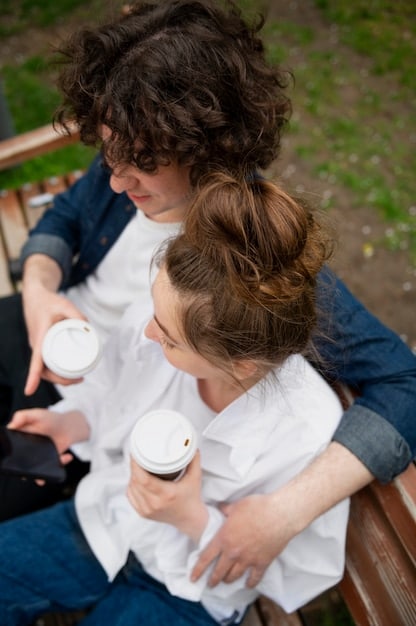 Two friends sitting on a park bench, both holding coffee cups and engaged in a heartfelt conversation. The background is blurred, focusing attention on their interaction.