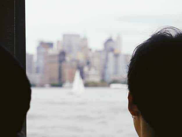 A person looking thoughtfully out a window, with a blurred cityscape in the background. The lighting is soft, creating a reflective and introspective mood. The image captures a moment of contemplation about one's social connections.