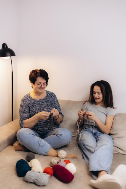 An older woman is teaching a young girl how to knit, both sitting comfortably in armchairs, with a warm, inviting living room setting.