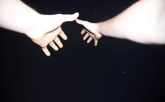 A close-up shot of two hands reaching out to each other, with a slight gap between them.  The background is blurred, suggesting a focus on connection and the effort to bridge a divide in a relationship. The setting is intimate but conveys a sense of longing and need for reconciliation.