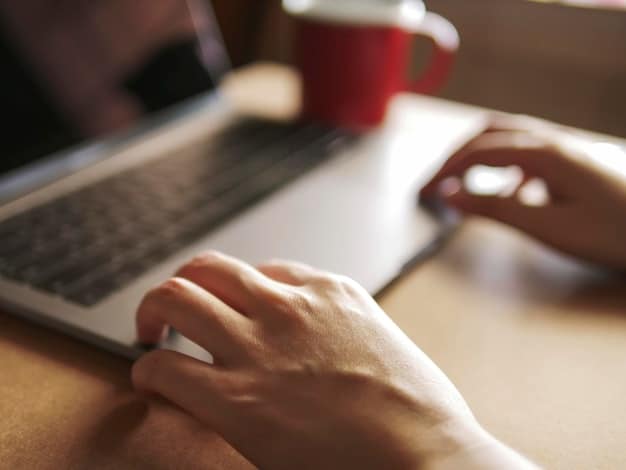 A close-up of a person's hand typing on a laptop, with a blurred background of abstract digital rules or guidelines, symbolizing the careful crafting and implementation of community rules for safety and order.