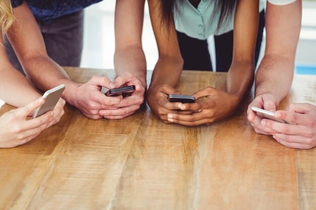 A close-up of a diverse group of US teenagers' hands holding smartphones, with social media apps visible on the screens. The background is slightly blurred, focusing on the interaction with the devices, conveying the omnipresence of digital engagement.